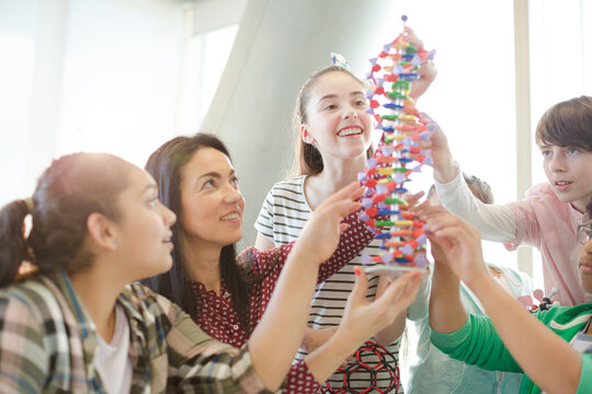 Female teacher and students examining DNA model in classroom