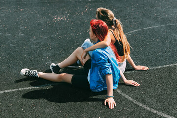 Teenage girls are sitting on a sports field in a park or a school stadium. Friends, friendship,...