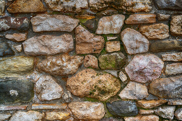 cobblestone wall, old and weathered, gray and brown covered with green moss