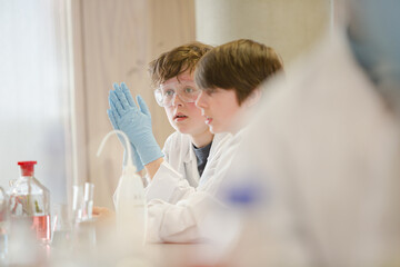 Boy students conducting scientific experiment, examining liquid in test tube in laboratory classroom