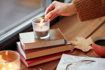 holidays and leisure concept - woman's hand with match lighting candle at home on halloween