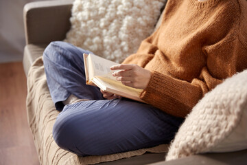 people, season and leisure concept - close up of woman in warm sweater reading book at home