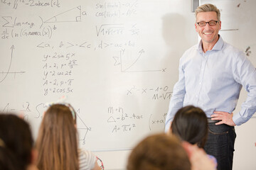 Male teacher leading lesson at whiteboard in classroom