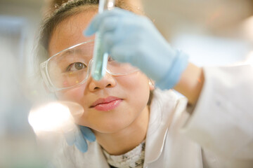 Girl students conducting scientific experiment, examining liquid in test tube in laboratory classroom
