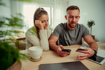 Caucasian happy couple making online payment sitting at kitchen table 