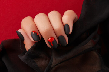 Close up womans hand with halloween manicure on red background holding fabric. Manicure, pedicure beauty salon concept