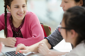 Female teacher and girl students using laptop in library