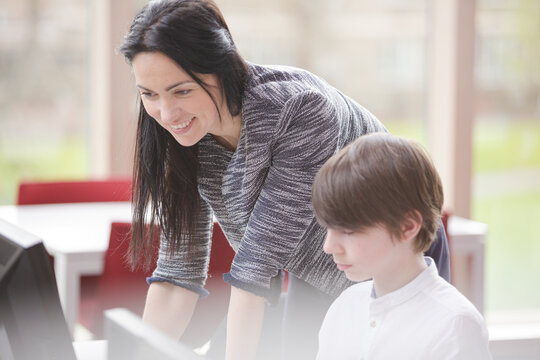Female teacher helping boy student at computer