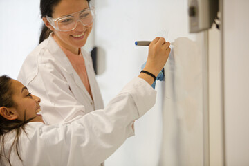 Female science teacher and girl student writing at whiteboard in classroom