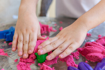 Closeup of child's hands playing in kinetic sand. Selective focus shot of kid's hands with red...