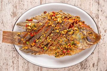 tasty large fried nile tilapia fish with chili, garlic and coriander in oval ceramic plate on white...