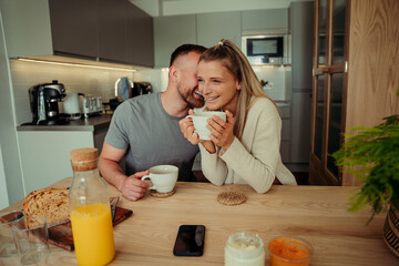 Caucasian happy couple sitting at kitchen table whispering in ear