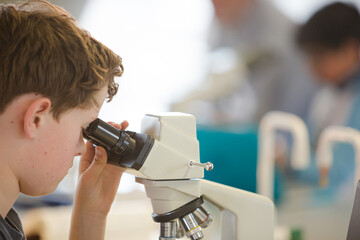 Boy student conducting scientific experiment at microscope and computer in laboratory classroom