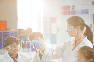 Obraz premium Female teacher and students examining liquid in test tube, conducting scientific experiment in laboratory classroom