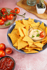 A blue bowl with cheese tortilla chips and a chilli cheese dip on a pink marble surface, cherry tomatoes, ketchup