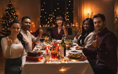 holidays, party and celebration concept - multiethnic group of happy friends having christmas dinner at home and showing thumbs up