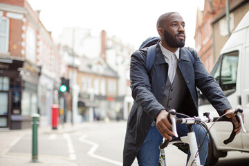 African businessman commuting, riding bicycle on urban street