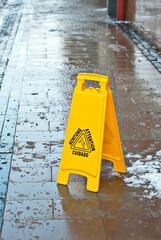 Yellow danger sign. Symbol of a slippery sidewalk. Inscription attention in different languages. Plate near the cobblestones in the spring.