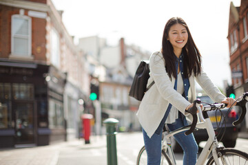 Portrait smiling young woman commuting, riding bicycle on sunny urban street