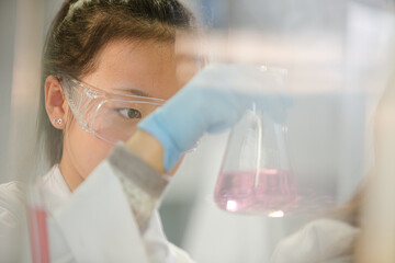 Girl student examining pink liquid, conducting scientific experiment in laboratory classroom