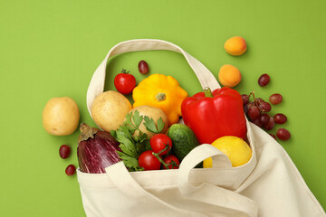 Cotton bag with vegetables and fruits on green background