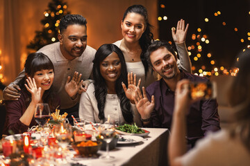 holidays, party and celebration concept - young woman taking picture on smartphone of her multiethnic group of happy friends while having christmas dinner at home