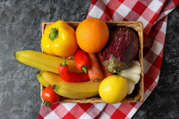 Basket with vegetables and fruits on kitchen towel on black smokey table