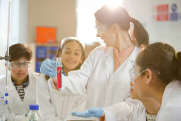 Obraz premium Female teacher and students conducting scientific experiment, watching liquid in test tube in laboratory classroom