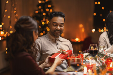 holidays, party and celebration concept - multiethnic group of happy friends having christmas dinner and giving presents at home