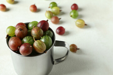 Cup of ripe gooseberry on white textured background