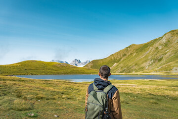 Young man on the top of a green mountain enjoying the amazing lake landscape views during sunset. Paradise grass mountain. Lifestyle relax and freedom. The beauty of nature concept.
