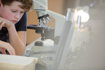 Boy student conducting scientific experiment at microscope and computer in laboratory classroom