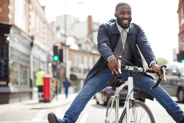 Fototapeta na wymiar Playful young businessman commuting, riding bicycle on urban street