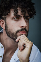 portrait of a young man with beard and curly hair, holding his chin with his hand and looking thoughtful