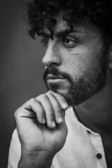 black and white portrait of a young man with beard and curly hair, holding his chin with his hand and looking thoughtful