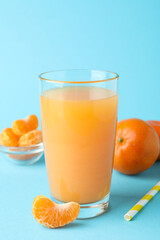 Glass of mandarin juice, straw and ingredients on blue background