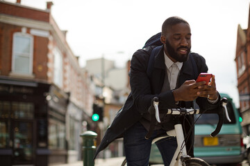 Young businessman commuting with bicycle, texting with cell phone on sunny urban street