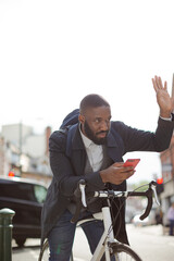 Young businessman commuting with bicycle, texting with cell phone on sunny urban street