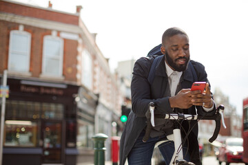 Young businessman commuting with bicycle, texting with cell phone on sunny urban street