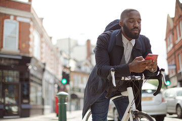 Fototapeta na wymiar Young businessman commuting with bicycle, texting with cell phone on sunny urban street