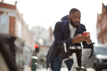 Young businessman commuting with bicycle, texting with cell phone on sunny urban street