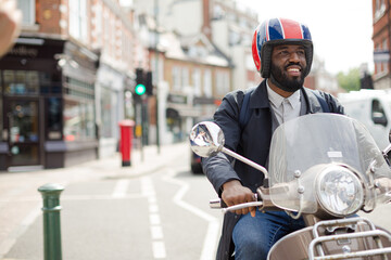 Smiling young businessman in helmet riding motor scooter on urban street