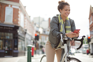 Young woman commuting on bicycle, texting with cell phone on sunny urban street
