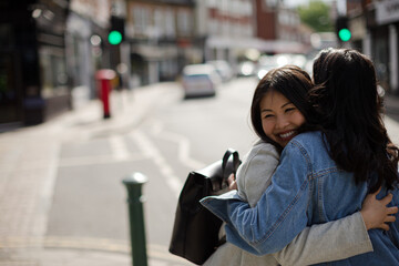 Smiling affectionate female friends hugging on sunny urban street