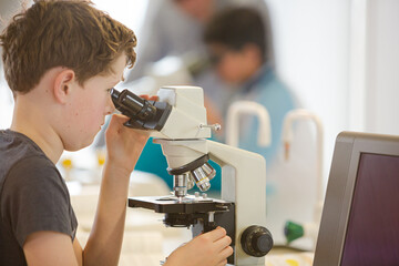 Boy student conducting scientific experiment at microscope and computer in laboratory classroom