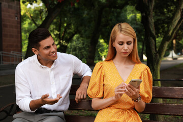 Young woman with smartphone ignoring her boyfriend in park. Boring date - obrazy, fototapety, plakaty