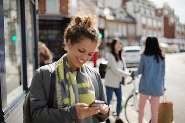 Young woman texting on sunny urban street
