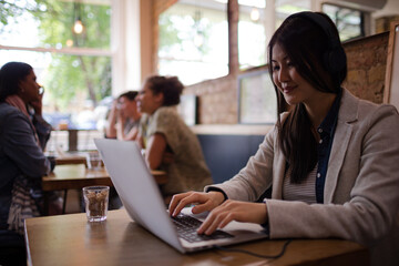 Young woman with headphones using laptop at cafe table