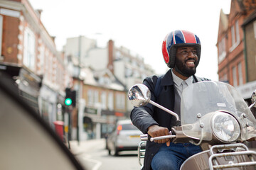 Smiling young businessman in helmet riding motor scooter on urban street