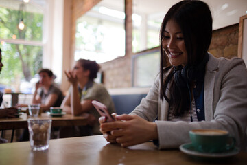 Obraz premium Young woman with headphones texting with cell phone and drinking coffee at cafe table